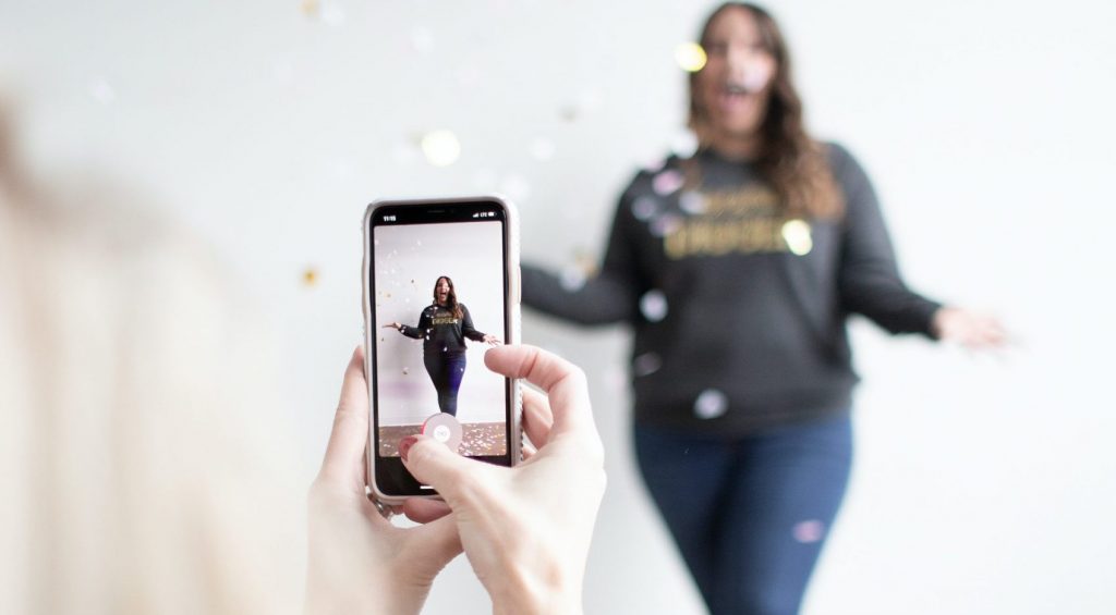 person holding white smartphone taking photo of woman wearing blue jeans