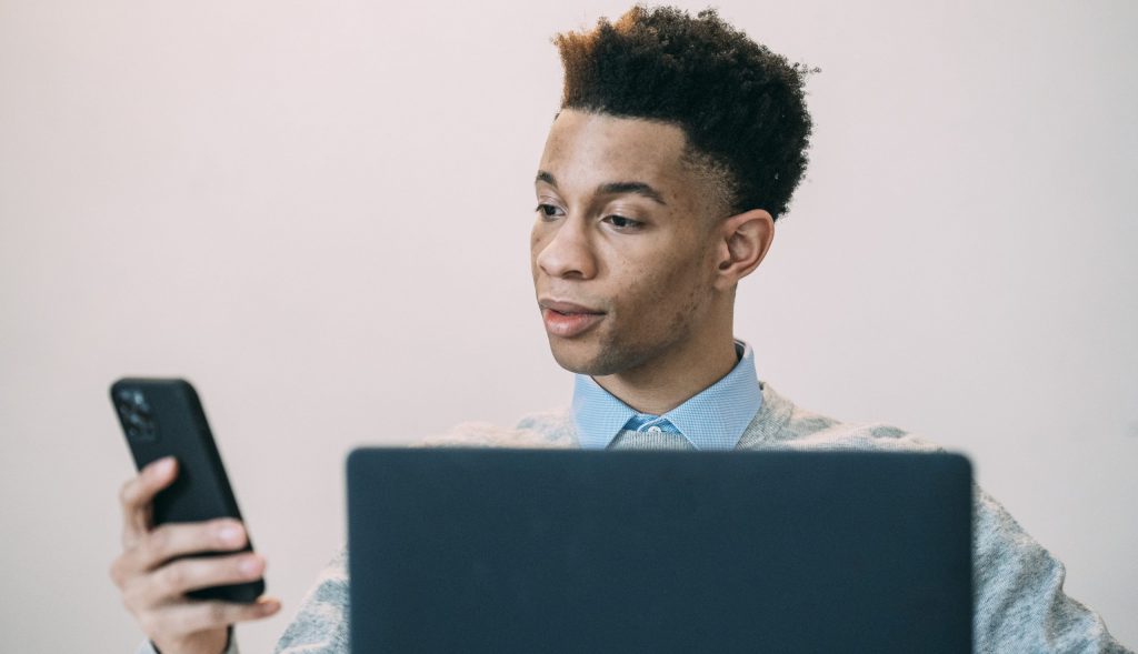 Black man browsing smartphone near laptop