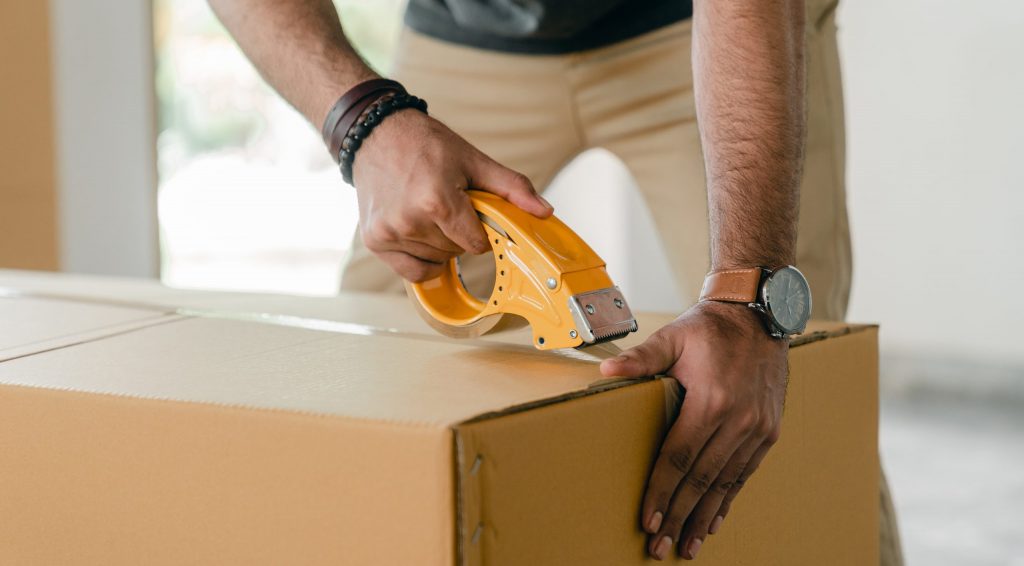 Crop man taping carrying box with scotch