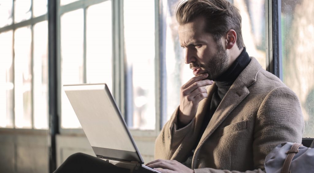 Man wearing brown jacket and using grey laptop