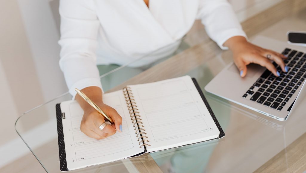 Person writing on notebook while using a laptop