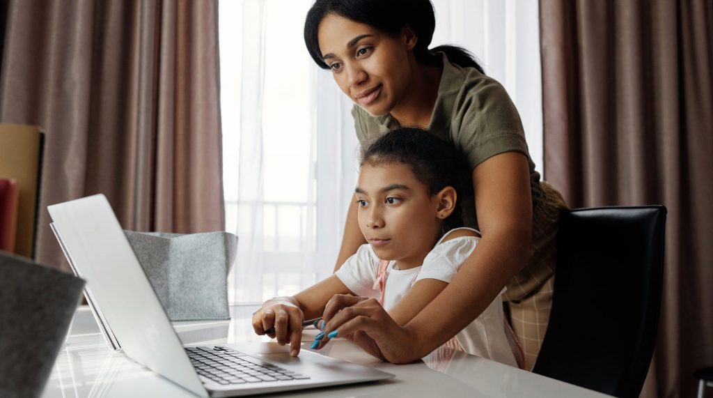 Mother helping her daughter use a laptop