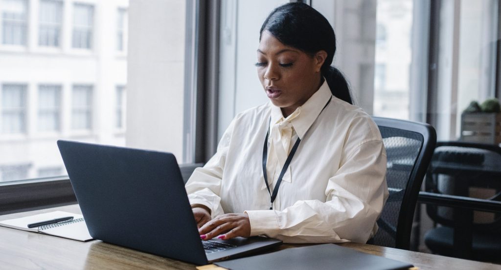 Serious black businesswoman typing text on laptop