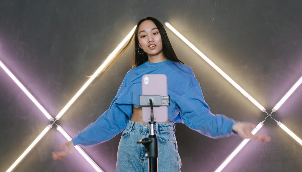 A woman in blue sweater dancing in front of her mobile phone on a tripod