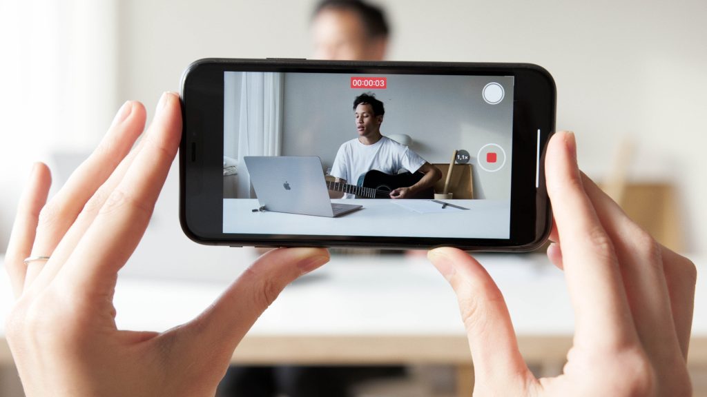 Person holding a smartphone recording a man playing guitar