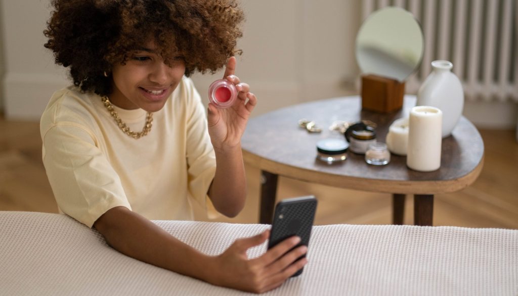 Woman in yellow shirt showing a beauty product while recording on smartphone