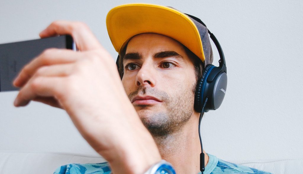 man wearing black corded headphones while holding phone