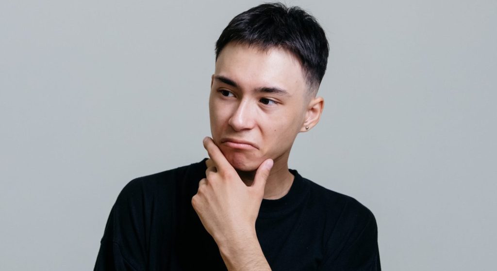 Man in black crew neck shirt thinking with his hand on his chin