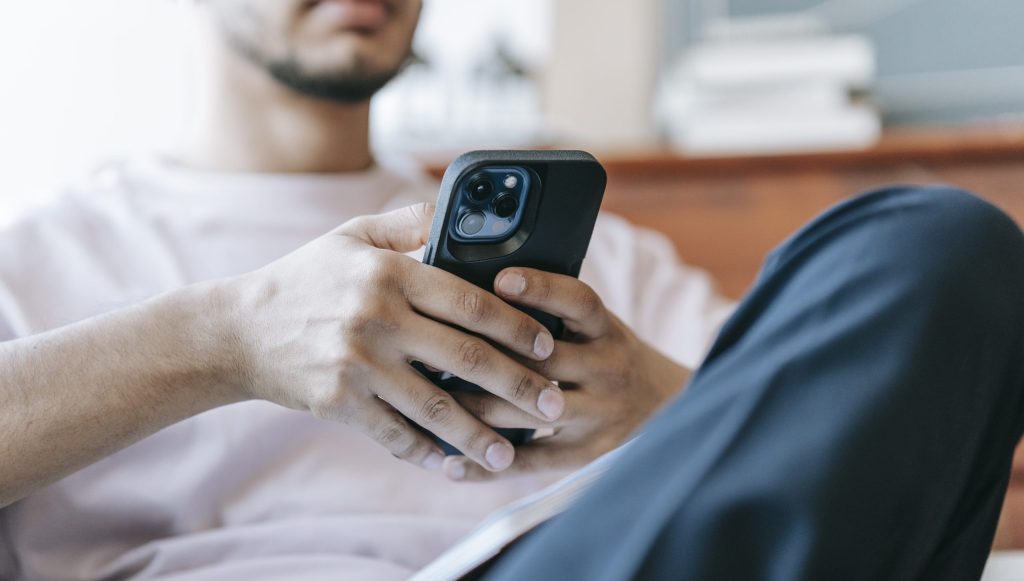 Crop bearded man using smartphone in living room